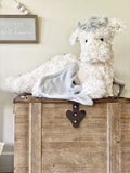 A plush dragon made by ClaraLoo with white and gray fur, sitting on top of a wooden trunk in a fantasy themed nursery.