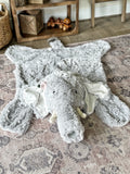 A gray elephant plush rug made by ClaraLoo. The elephant rug is made from faux fur, with crochet tusks and a crochet snout.