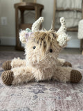 A plush highland cow stuffed animal with tan faux fur. This highland cow is handmade by ClaraLoo with crocheted accents.