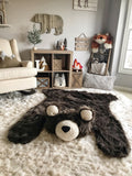 A large brown bear rug on a cream colored carpet in a woodland themed bedroom. The bear rug is made by ClaraLoo with plush faux fur. The animal rug has cream colored ears and face with a black nose.