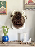 A plush Bison Wall Mount handmade by ClaraLoo in a western themed cowboy nursery. The stuffed bison is made of soft brown faux fur with cream colored crocheted ears and horns.  The bison is mounted on a white wooden plaque.