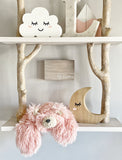 A plush pink bear lovey resting on a white shelf. The bear lovey is made by ClaraLoo with soft faux fur and crochet accents.